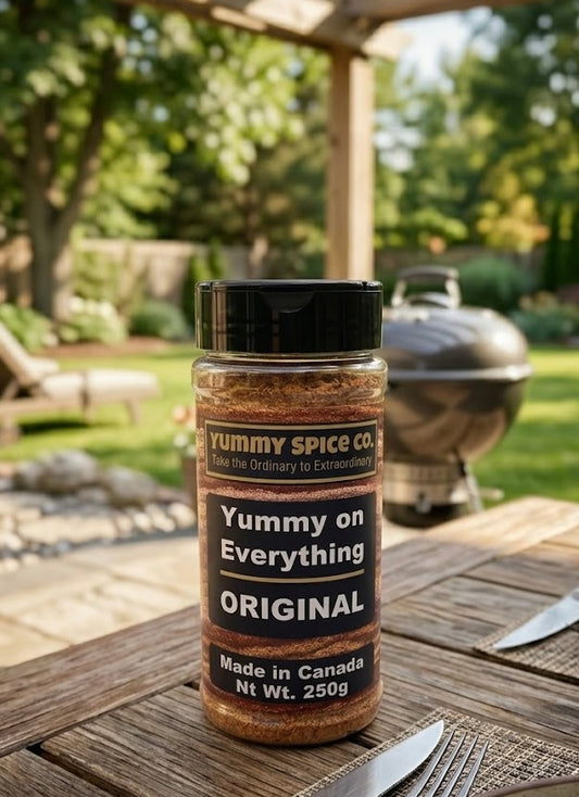 Yummy Spice Co. seasoning bottle on a wooden table with a grill and garden in the background